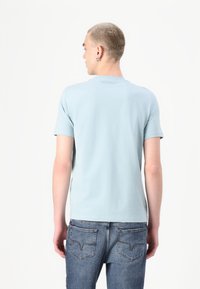 Ανοιχτό μπλε βαμβακερό μπλουζάκι με κοντό μανίκι, σχεδίαση με λαιμόκοψη, διακριτική λεπτομέρεια μάρκας στην πλάτη, σε συνδυασμό με τζιν παντελόνι μέτριου πλυσίματος.