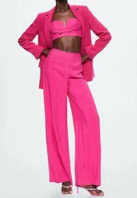 Costume fuchsia comprenant un haut ajusté et court avec un détail en nœud et un pantalon à jambes larges. Tissu lisse avec une coupe sur mesure et un design élégant.