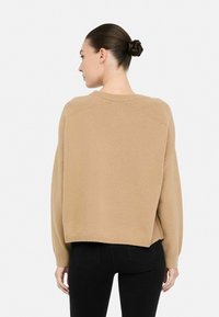 Maglione marrone a maglia con una vestibilità ampia, dettagli a coste sulle spalle e orlo arrotondato, abbinato a jeans neri.