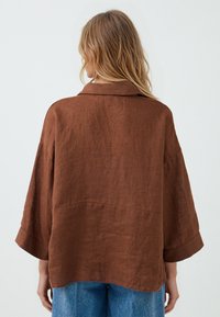 Camicia in lino marrone con vestibilità rilassata, dotata di collo e maniche ampie, progettata con una sottile trama e dettagli cuciti.