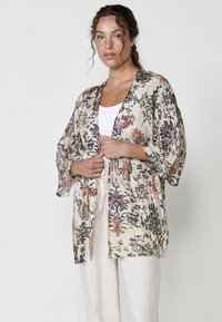Kimono ligero con estampado floral en beige, que presenta mangas anchas y un diseño de frente abierto. Tejido de lino texturizado con acentos vibrantes.