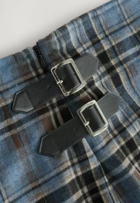 Blau- und schwarz kariertes Gewebe mit zwei schwarzen Lederträgern, die mit silbernen Metall-Schnallen versehen sind, an einem Reißverschlussverschluss. Strukturierter und gemusterter Entwurf.