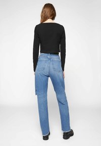 Top preto de mangas longas combinado com jeans de perna reta azul claro. Os jeans apresentam um leve efeito de desgaste e uma bainha desfiada. Botas pretas de tornozelo completam o visual.