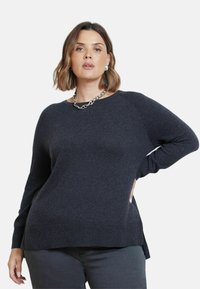 Mörkgrå tröja i mjukt stickat material, med rundad halsringning, långa ärmar, sidoflikar och en avslappnad passform.