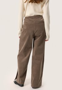Brown corduroy wide-leg pants with side slits at the hem. Designed with a high waist and textured fabric for a structured look.