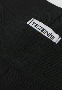 Czarna tkanina o gładkiej fakturze ma naszytą metkę z napisem "TEZENIS" w kolorowej czcionce na białym tle.