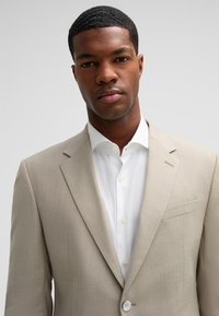 Beige Leinenblazer mit Reverskragen und einem einzigen Knopfverschluss, kombiniert mit einem weißen Hemd mit spitzem Kragen.