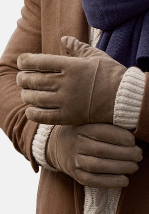 Brune ruskindshandsker med en glat tekstur har fire tydelige fingeråbninger og enkle syninger, suppleret af en cremefarvet striktrøje.