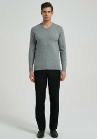 Pull gris à manches longues et col en V en tricot doux, associé à un pantalon noir à jambes droites et des chaussures noires. Design simple.
