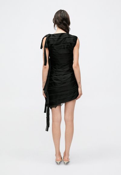 Čierne saténové šaty s textúrovanými vertikálnymi záhybmi, asymetrickým lemom, čipkovou ozdobou na spodnej časti a jedným ramienkom s viazaním.