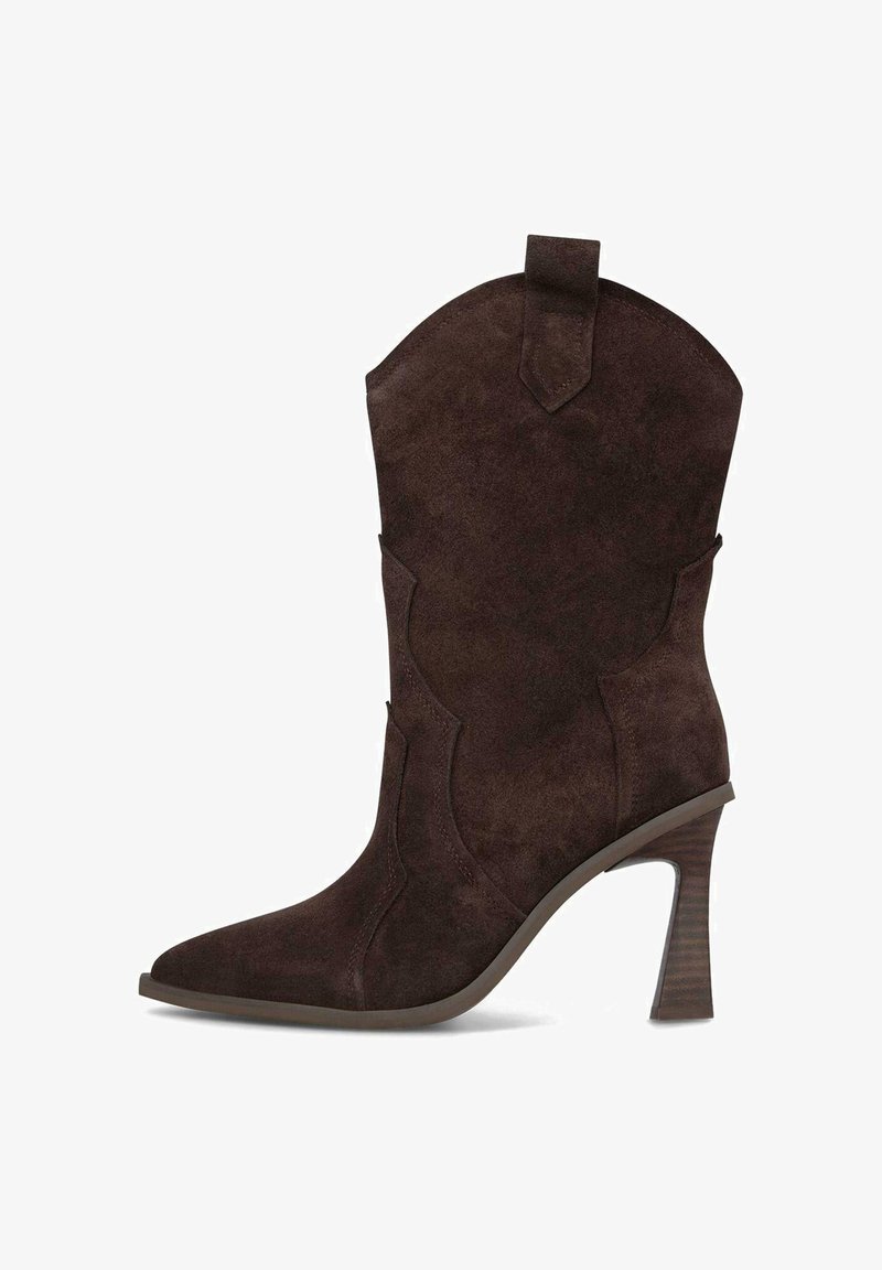 Botín de ante marrón hasta el tobillo con punta afilada, caña curva y costuras decorativas. Presenta un alto tacón apilado y una lengüeta en la parte superior.
