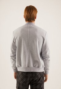Sudadera gris con un tejido texturizado, cuello redondo y puños acanalados; presenta una costura central que recorre la espalda. Combinada con pantalones de cuadros.