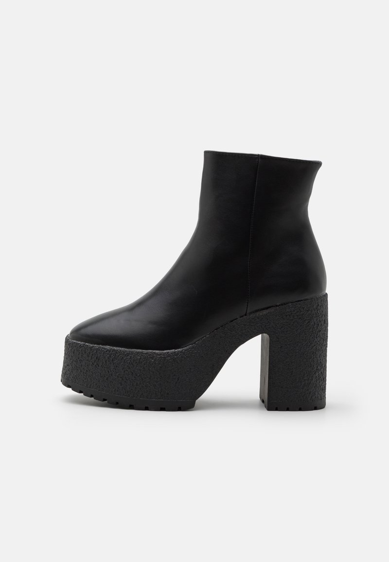 Botte noire en cuir à la cheville avec un bout pointu, une semelle plateforme texturée et un épais talon bloc. Tige lisse avec des détails de couture minimalistes.