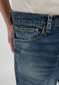 Blå denimjeans med medelhög midja, synlig sömnad och femficksdesign. Lätt sliten textur med koppardetaljer.