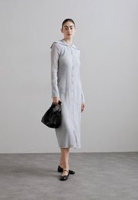 Long gray button-up dress with a hood, textured fabric, and long sleeves. Paired with black flat shoes and a small black handbag.