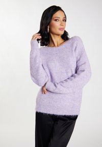Fliederfarbener, flauschiger Pullover aus weichlichem Material mit lockerer Passform, gerippten Bündchen und weitem Halsausschnitt, kombiniert mit glänzenden schwarzen Hosen.