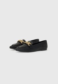 Sorte skinnloafers med spiss tå og en bred stropp med gullkjede-detalj foran. Flatt såle, minimalistisk design.