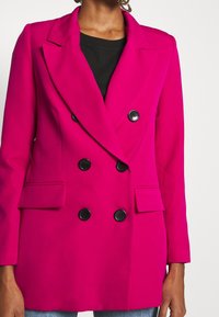 Fuchsie dvouřadé sako s černými knoflíky, klopy s výstřihem ve tvaru zářezu, bočními kapsami a střih přizpůsobený na postavu, kombinované s černou košilí pod ním.