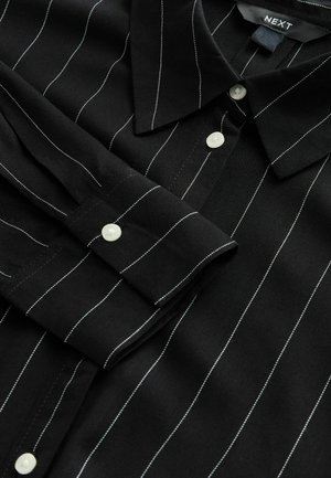 Black shirt with white vertical stripes, featuring a pointed collar, long sleeves, and white buttons at the cuffs and front placket.