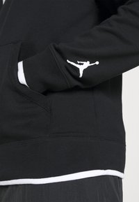 Felpa con cappuccio nera che presenta un logo Jumpman bianco sulla manica, una tasca a marsupio e una fodera bianca all'orlo per un contrasto aggiuntivo.