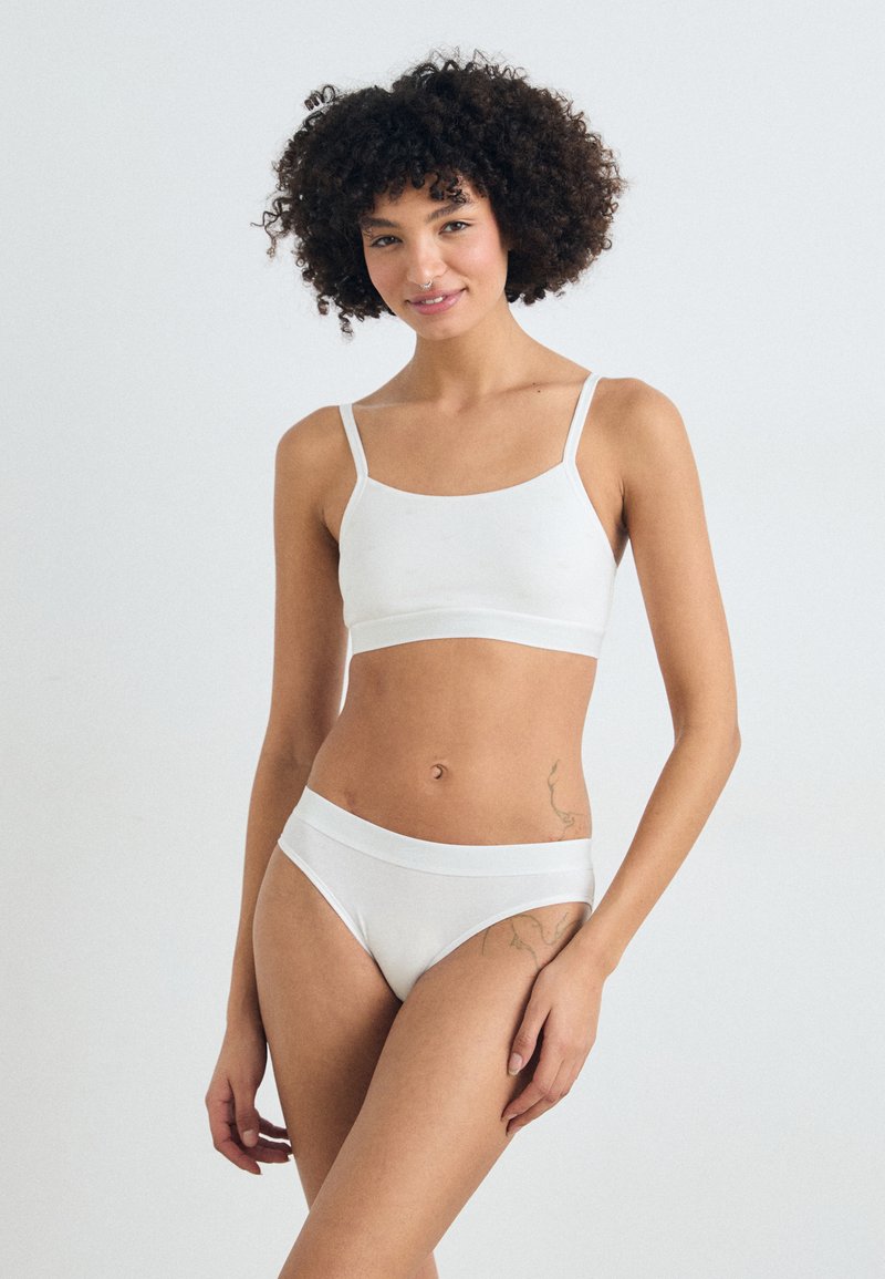 Bralette bianco in misto cotone con spalline sottili e scollatura arrotondata, abbinato a slip bikini bianchi senza cuciture. Texture liscia.