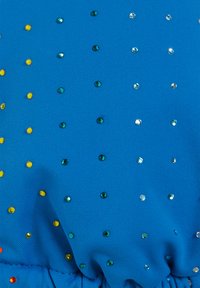 Kirkas sininen kangas, jossa on ripoteltuja kiiltäviä paljetteja vihreänä, keltaisena ja hopeana. Yhdessä on rynkytetty helma, joka luo tekstuurimaisen ilmeen.