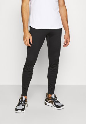 Leggings da palestra neri con vestibilità slim e texture liscia, abbinati a scarpe da ginnastica nere e grigie con dettagli gialli.