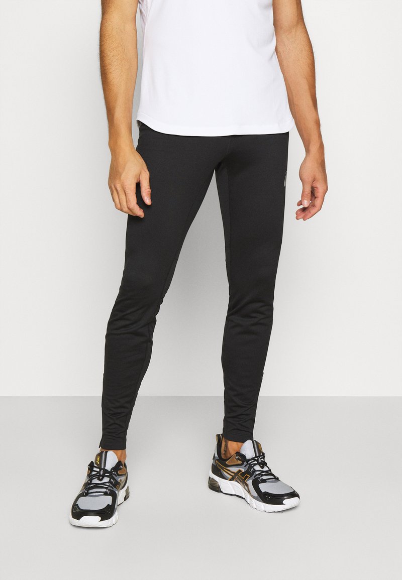 Schwarze Sportleggings mit schmaler Passform und glatter Textur, kombiniert mit schwarzen und grauen Sportschuhen mit gelben Akzenten.