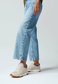 Beige sportschoenen met grijze accenten, geperforeerd ontwerp en bruine zool, gedragen met lichtblauwe high-waisted jeans.