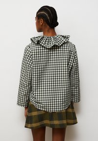 Zeleni i bijeli gingham top s naboranim ovratnikom, uparen s kariranom suknjom s žutim detaljima. Tekstura izgleda kao pamuk.