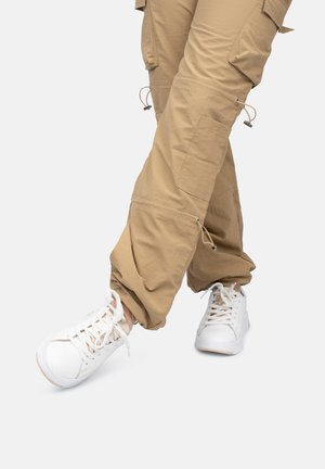 Beige cargobroeken met meerdere zakken, gesnoerd bij de enkels, gecombineerd met witte sneakers met een textuurdesign en vetersluiting.