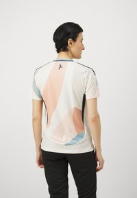 Kortærmet sports t-shirt i hvid, med abstrakte former i fersken, blå og sort; mesh tekstur og logo detalje på ryggen.