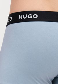 Világoskék boxeralsó, puha, fekete elasztikus derékpánttal, rajta fehér "HUGO" felirattal. Sima szövetanyag és testhezálló dizájn.