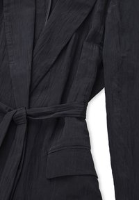 Giacca nera textured con cintura, revers a punta e tasca a toppa, caratterizzata da un tessuto stropicciato che aggiunge profondità al design.