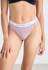 Chiloți thong roz cu modele florale negre și o talie elastică albă pe care se află logo-ul "Tommy Hilfiger".