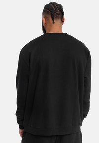 Sudadera negra de algodón; presenta un corte holgado, puños acanalados y escote redondeado. Diseño simple sin patrones ni acentos visibles.