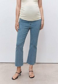 Jeans de un azul claro con una forma ligeramente acampanada, dobladillo sin terminar y bolsillos, combinados con un top ajustado color crema y tacones negros con tiras.