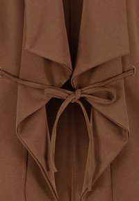 Brun omslagjacka med draperad front, knytstängning och mjuk tygkvalitet. Har en öppen krage och en strukturerad silhuett.