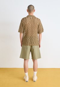 Short-sleeve, brown, textured knit shirt with zigzag pattern; paired with light green shorts and white socks. Background is yellow.