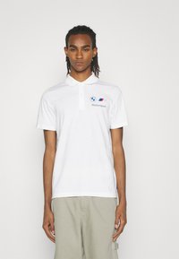 Hvid bomulds polo shirt med krave, korte ærmer og et Motorsport-logo på venstre bryst med farverige striber nedenfor.