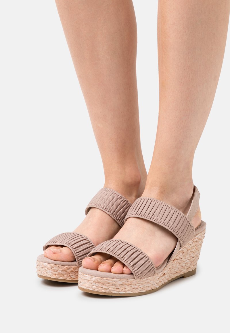 Beige kilehæle sandaler med ribbet stofremme og en vævet jutesål. Har åbne tæer og to justerbare ankelremme for støtte.