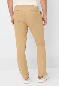 Beige katoenen chinos met een slim fit, voorzien van twee achterzakken met knoopsluitingen en zijzakken, gecombineerd met lichte sneakers.