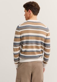 Sweter w paski w brązowe, białe i niebieskie poziome pasy, o prążkowanej strukturze i okrągłym dekolcie. W połączeniu z beżowymi spodniami cargo.