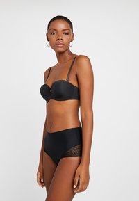 Completo di lingerie nero composto da un reggiseno imbottito senza spalline in tessuto liscio e un perizoma a vita alta con dettagli in pizzo sui lati.