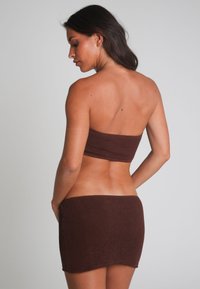 Haut de bikini tricoté marron et mini jupe, présentant un motif texturé. Le haut est sans bretelles et la jupe se positionne sur les hanches.