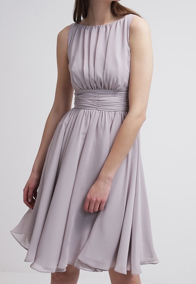 Robe sans manches, de couleur violet clair, longueur genou, avec taille froncée et corsage plissé, portée par une femme sur un fond uni.