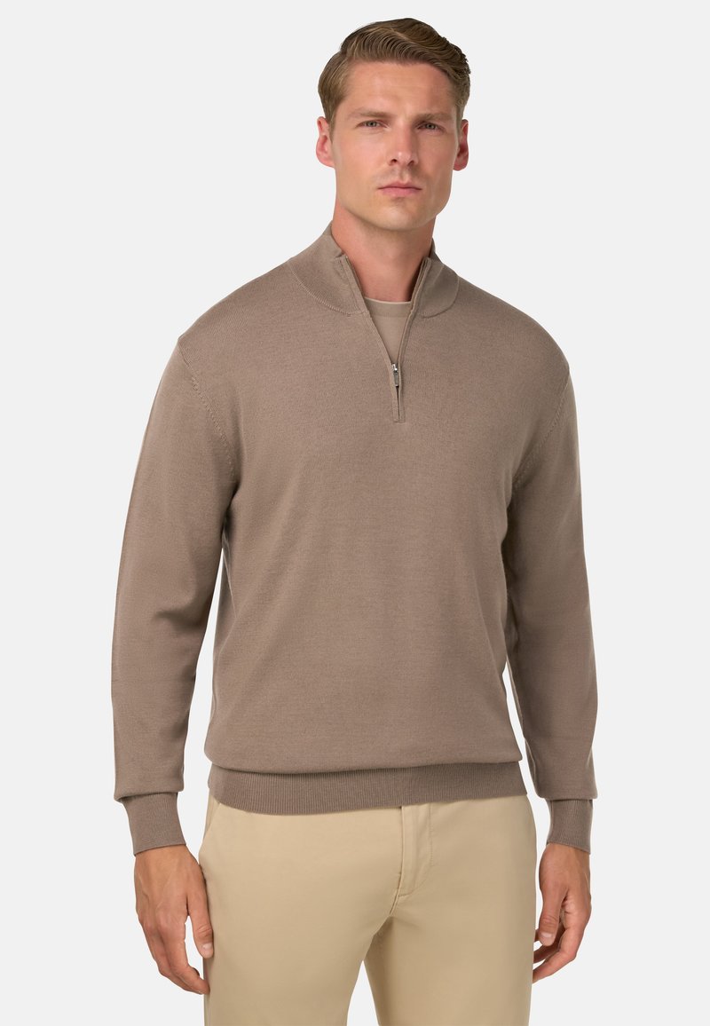 Hellbrauner Pullover mit halbem Reißverschluss und langen Ärmeln, gerippten Bündchen und Saum, der eine glatte Strickstruktur aufweist. Trägt man über einer helleren Basisschicht.