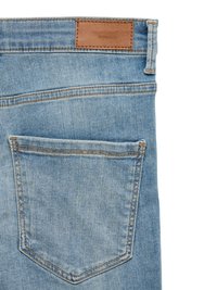 Back view of light blue denim jeans pocket with brown leather brand patch and visible stitching.