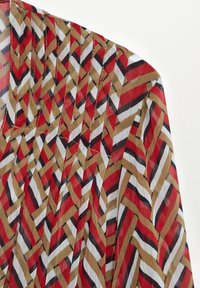 Tissu avec un motif géométrique de bandes diagonales entrelacées en rouge, beige, noir et blanc, avec des coutures détaillées le long de la couture.