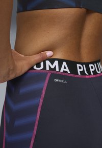 Fascia elastica nera con logo "PUMA", tessuto grigio scuro con motivo a freccia blu, dettaglio di cucitura rosa, etichettato "DRYCELL".